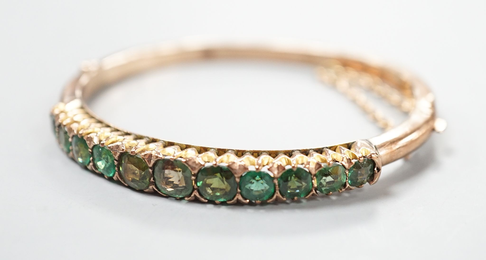 An Edwardian 9ct and graduated eleven green stone doublet set hinged bracelet, interior diameter 56mm, gross 12.6 grams.